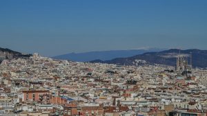 Aerial shot of Barcelona's cityscape featuring La Sagrada Familia and distant mountains.