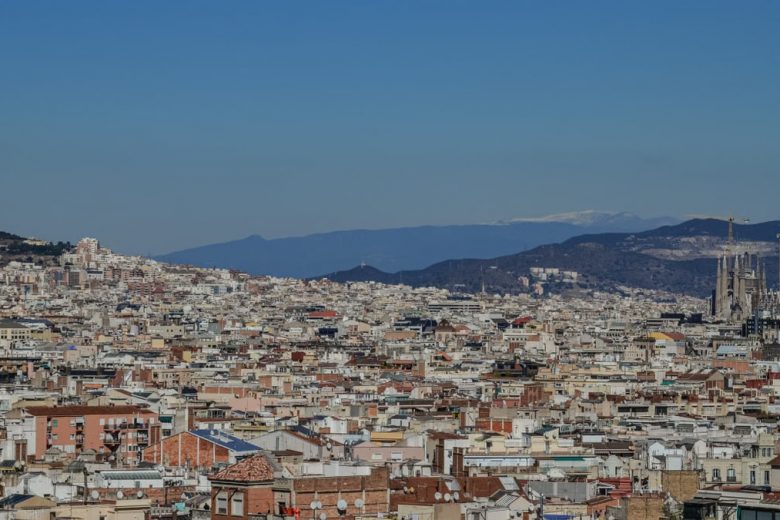 Aerial shot of Barcelona's cityscape featuring La Sagrada Familia and distant mountains.